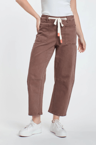 Woman wearing brown relaxed fit utility pants with a white drawstring waist and white sneakers.
