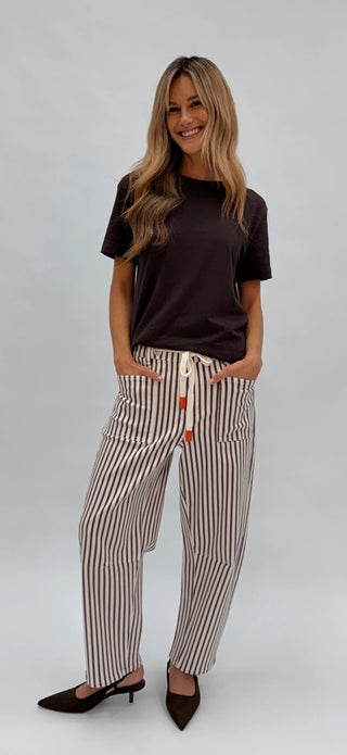 Woman smiling in brown t-shirt and striped linen drawstring pants with kitten heels.
