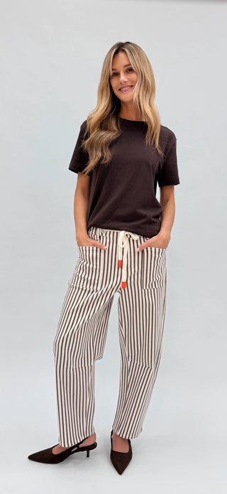 Woman wearing a dark brown t-shirt and striped linen lounge pants with black heels.