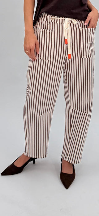 Woman wearing brown and white vertical striped linen pants with a drawstring waist and black heels.