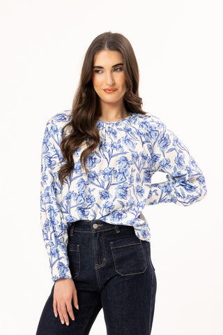 Woman wearing a blue and white floral print long sleeve blouse and dark denim jeans.