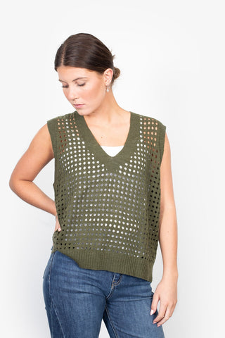 Woman wearing an olive green crochet knit sleeveless V-neck vest and blue denim jeans.