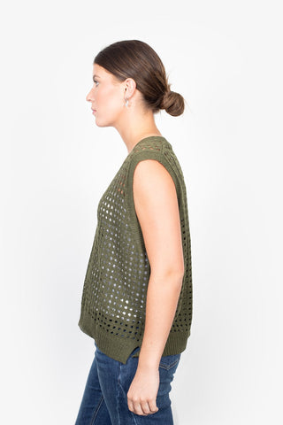 Woman in profile wearing an olive green crochet sleeveless knit top and blue jeans