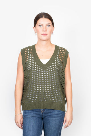 Woman wearing an olive green crochet knit sleeveless vest over a white top and blue jeans.