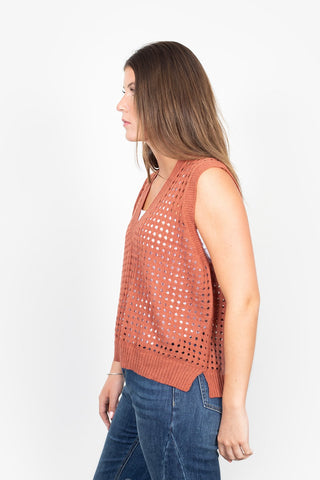 Woman wearing a rust-colored crochet knit sleeveless vest and blue jeans.