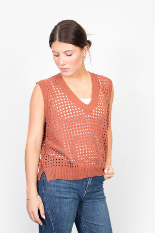 Woman wearing a rust orange crochet knit sweater vest and blue denim jeans.