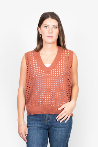 Woman wearing a rust orange crochet knit sleeveless V-neck vest and blue denim jeans.