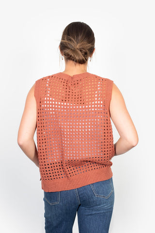 Back view of a woman wearing a terracotta orange crochet knit sleeveless top and blue jeans.
