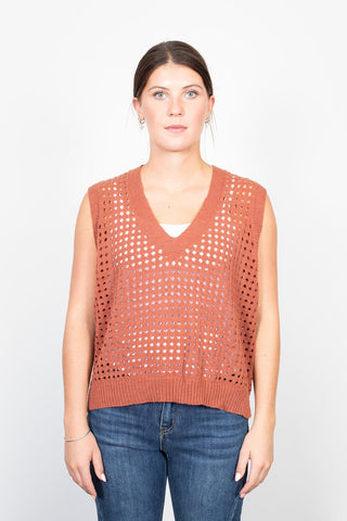 Woman wearing a rust-colored knit sleeveless vest and blue denim jeans.