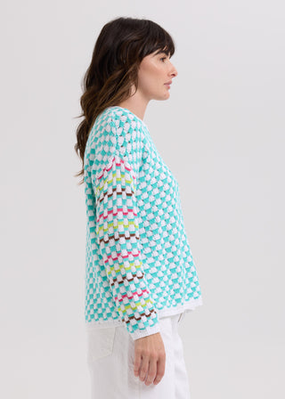 Woman in profile wearing a teal and white textured knit cardigan with rainbow striped sleeves.