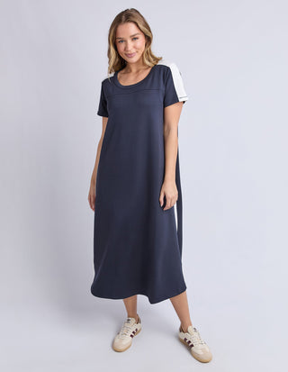 Woman wearing a navy blue short sleeve midi dress with white shoulder accents and sneakers.