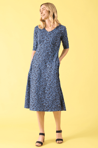 Woman wearing a blue and light blue patterned midi dress with black heels against a yellow background