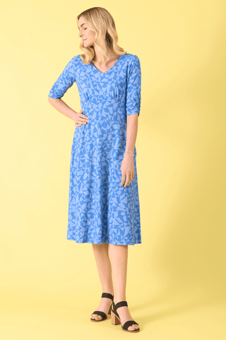 Woman wearing a blue patterned midi dress and black block heels against a yellow background