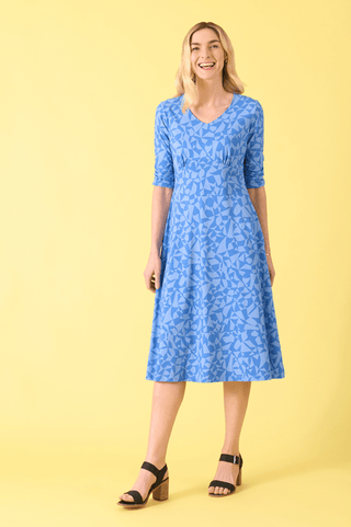 Smiling blonde woman wearing a blue geometric print midi dress and black block heels.