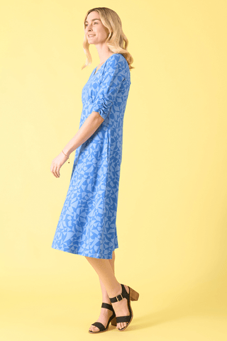 Woman wearing a blue geometric print midi dress and black block-heel sandals.