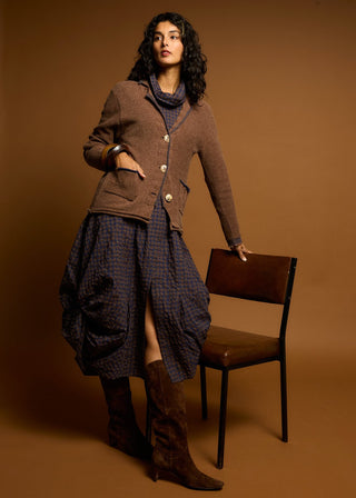 Woman wearing a brown textured jacket, patterned midi skirt, and tall brown boots.