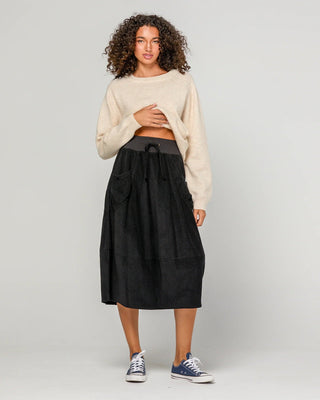 Woman wearing a cream knit sweater and black midi skirt with drawstring waist.