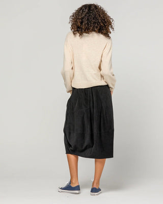 Woman wearing a cream knit sweater and black midi skirt with blue canvas sneakers.