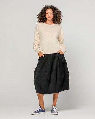 Woman wearing a cream knit sweater and a black midi skirt with pockets.