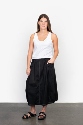 Woman wearing a white tank top and black maxi skirt with black sandals.