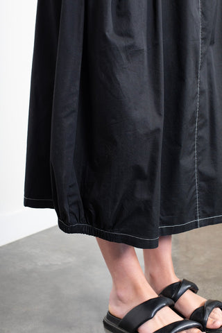 Woman wearing a black midi skirt with white contrast stitching and black leather sandals.