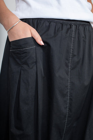 Woman wearing a black skirt with white contrast stitching and side pockets.