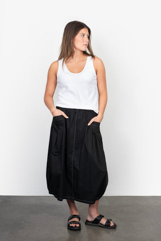 Woman wearing a white tank top and long black maxi skirt with pockets and black sandals.