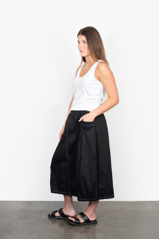 Woman wearing a white tank top and black wide-leg maxi skirt with white stitching.