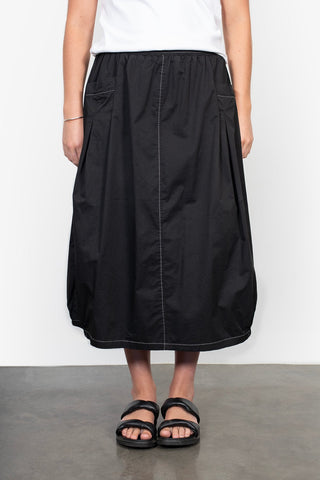 Woman wearing a black midi skirt with white contrast stitching and black slide sandals.