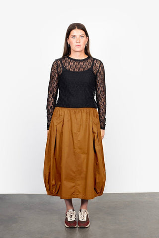 Woman wearing a black long-sleeve lace top and a brown voluminous midi skirt.