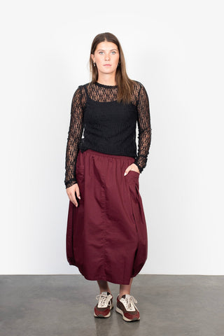 Woman wearing a black lace long sleeve top and a maroon maxi skirt with sneakers.