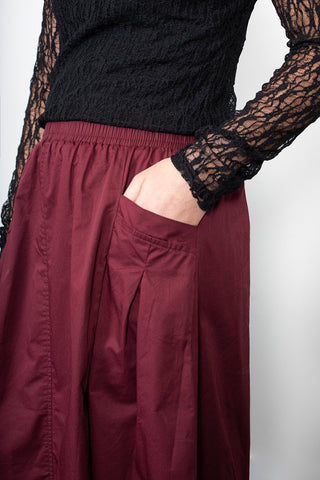 Woman wearing a black lace long sleeve top and burgundy pleated wide-leg pants.