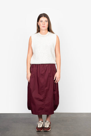 Woman wearing a white fuzzy sleeveless knit top and a long burgundy maxi skirt with sneakers.