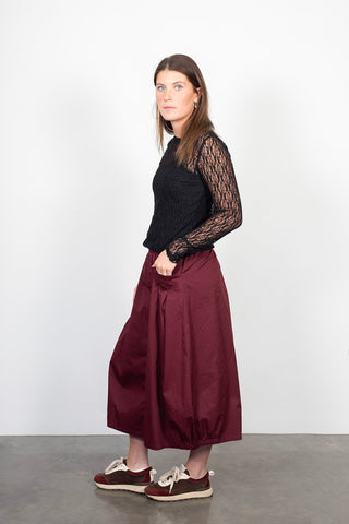 Woman wearing a black long-sleeve lace top and burgundy maxi skirt with casual sneakers.