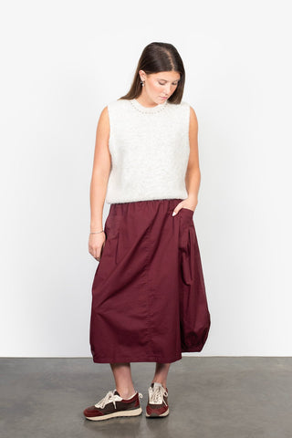 Woman wearing a white fuzzy sleeveless top and maroon midi skirt with sneakers.