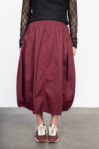 Woman wearing a burgundy midi balloon skirt with an elastic waist and black lace long sleeve top.