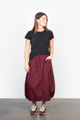 Woman wearing a black t-shirt and long burgundy maxi skirt with casual sneakers.