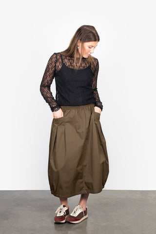Woman wearing a black lace long sleeve top and olive green midi skirt with pockets.