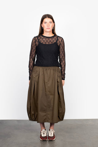 Woman wearing a black long sleeve lace top and olive green midi skirt with sneakers.