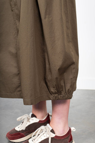Woman wearing olive green wide-leg pants and brown suede sneakers with white laces.