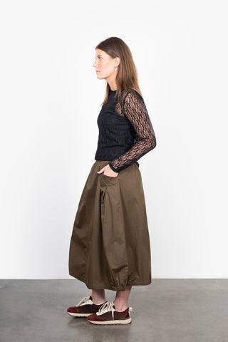 Woman wearing a black lace long sleeve top and olive green maxi skirt with pockets.