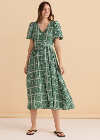 Woman wearing a green patterned midi dress with short puff sleeves and V-neckline.