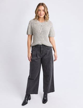 Woman wearing a grey textured short sleeve cardigan and wide leg dark grey trousers.