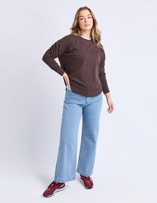 Woman wearing a brown oversized sweatshirt, light blue wide leg jeans, and red sneakers.