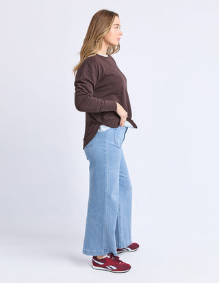 Woman wearing a brown sweatshirt, light blue wide-leg jeans, and red sneakers.