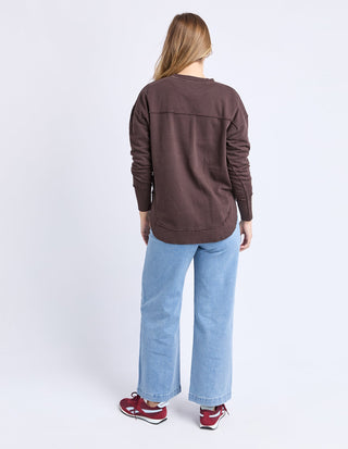 Back view of a woman wearing a brown long-sleeve sweatshirt, light blue wide-leg jeans, and red sneakers.