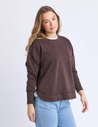 Woman wearing a brown long-sleeve sweatshirt with raw hem and light blue jeans.