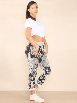 Woman wearing a white knotted t-shirt and black floral print apartment pants with sneakers.