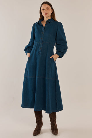 Woman wearing a long-sleeved dark blue denim tiered maxi dress and brown boots.