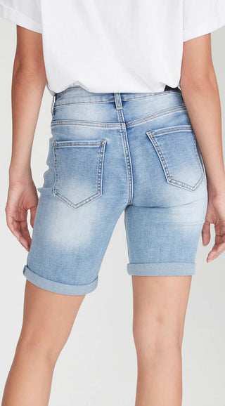 Back view of a woman wearing light wash denim shorts with rolled cuffs.